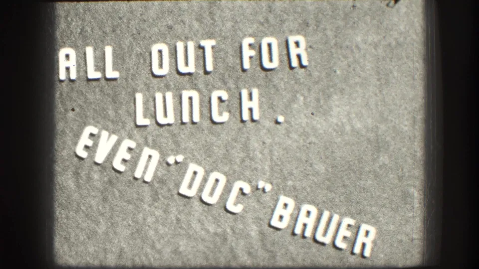 Close 8mm frame of the Kansas 1958 lunch title card, with white letters on a gray surface and visible film grain.