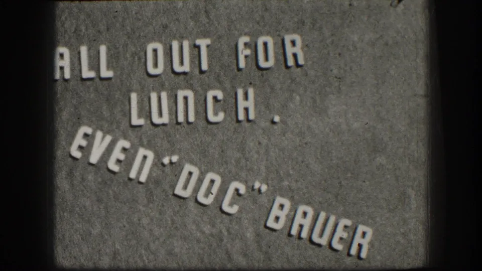 Darker 1958 Kansas 8mm title-card frame showing the lunch-break message and "Doc" Bauer name in raised white letters.