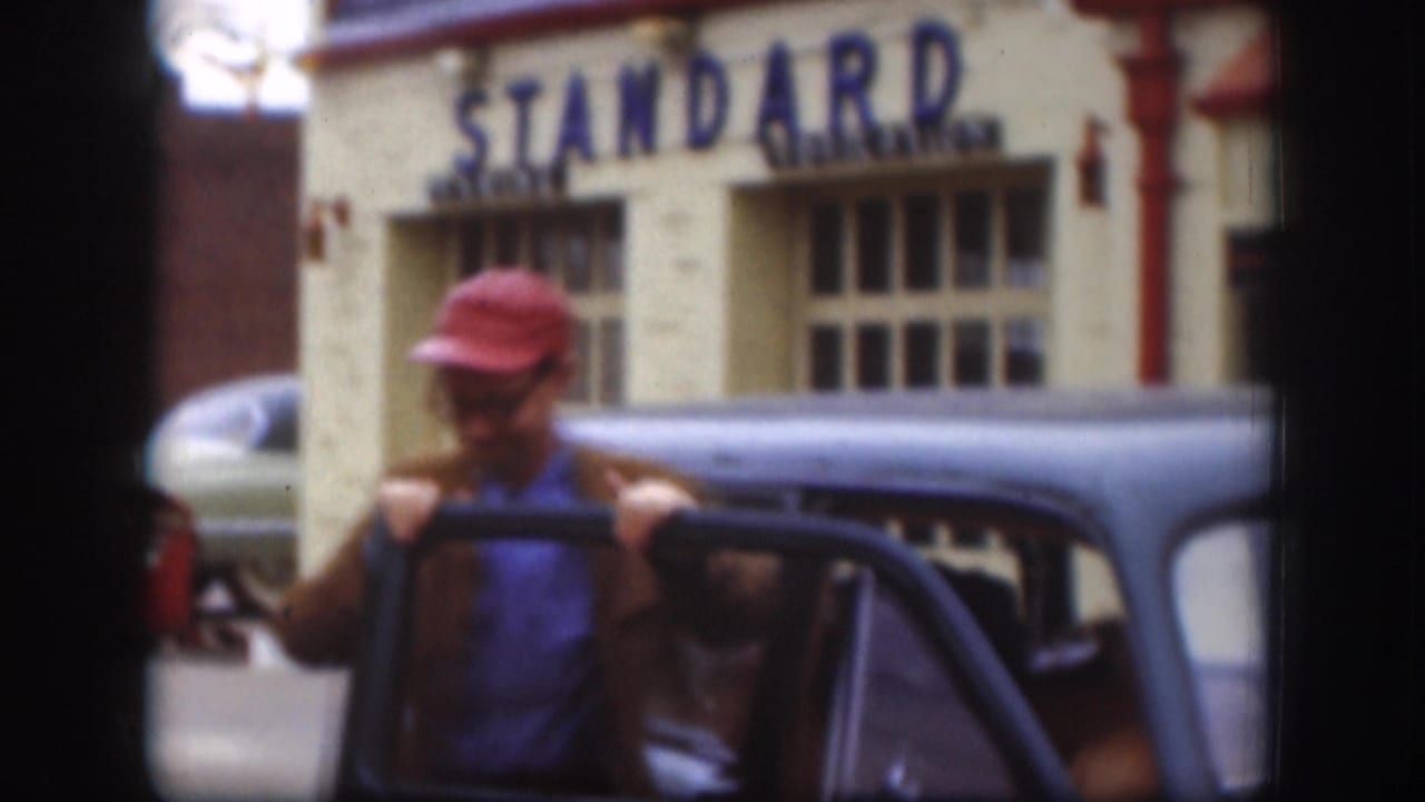 In 1958 Kansas footage, a man in a red cap stands by an open dark car door in front of a building with STANDARD lettering.