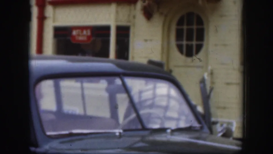 The 1958 Kansas street view shows the front of a dark vintage car against a cream building with red signage and an arched window detail.