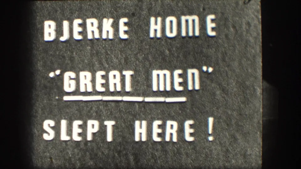 Close 8mm view of a stone plaque reading Bjerke Home, Great Men Slept Here, with textured surface and dark frame edges.