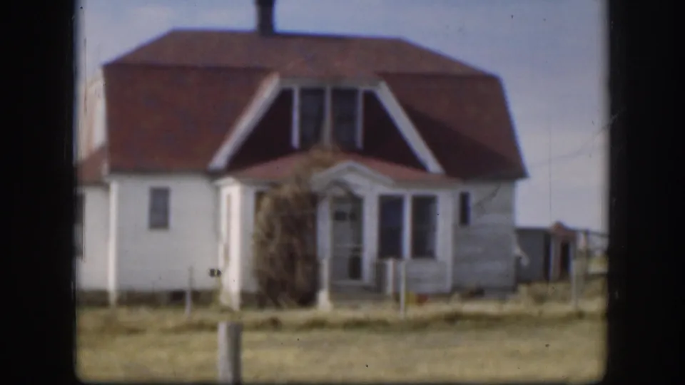 1958 Kansas 8mm frame showing a white two-story rural house with red roof, dormer windows, porch, grass, and clear sky.