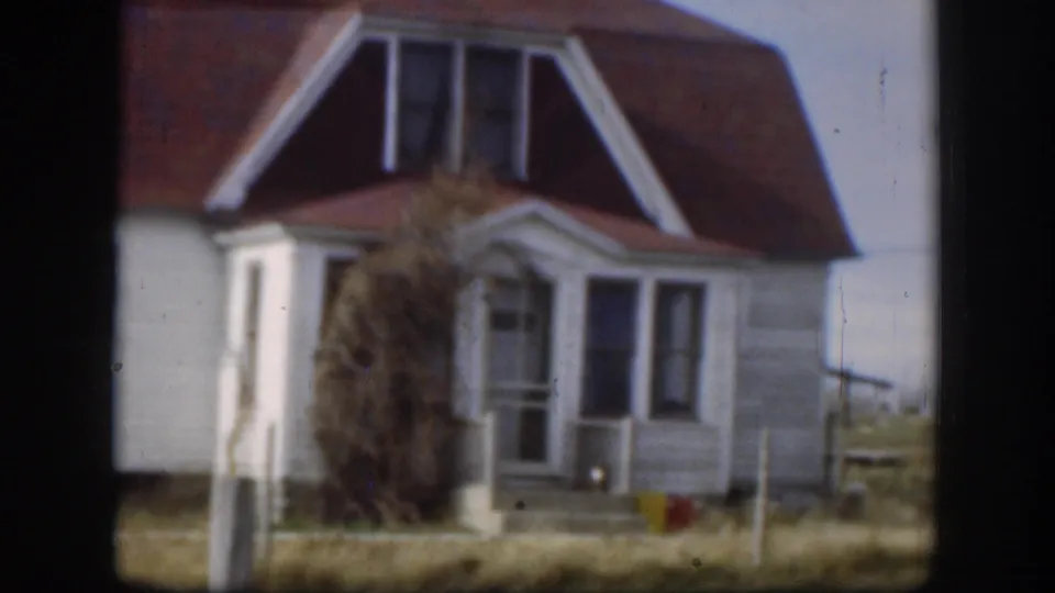 Closer 1958 Kansas view of the red-roofed white house, with porch details and yard posts visible.