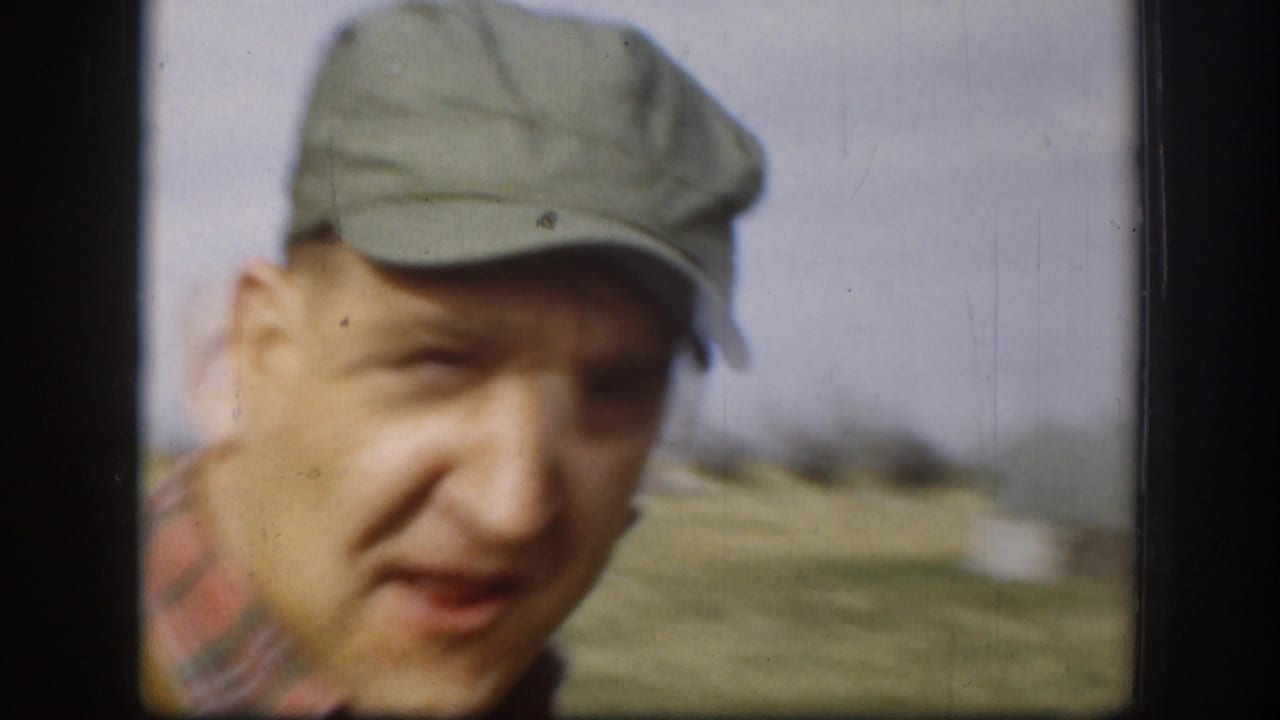 Adult man in a pale cap appears close to the camera outdoors in rural Kansas home-movie footage from 1958.