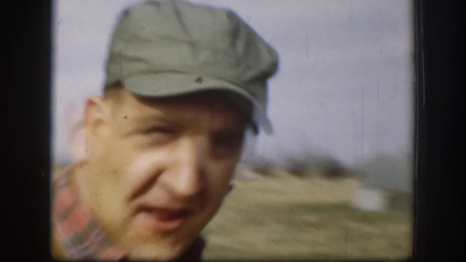 Adult man in a pale cap appears close to the camera outdoors in rural Kansas home-movie footage from 1958.