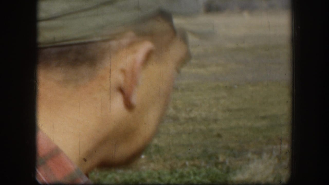 Side view of an adult man in cap and plaid shirt walking across a grassy rural area in 1958 Kansas footage.