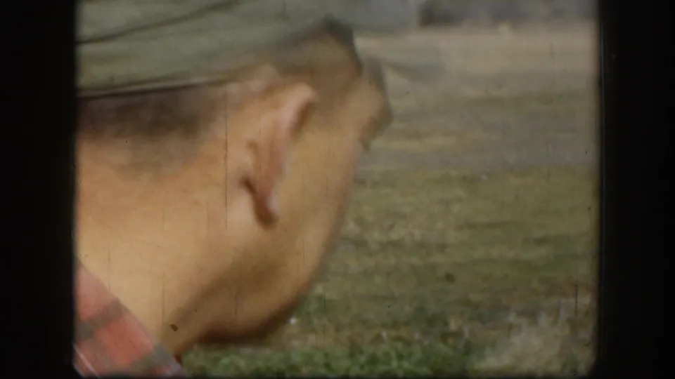 Side view of an adult man in cap and plaid shirt walking across a grassy rural area in 1958 Kansas footage.