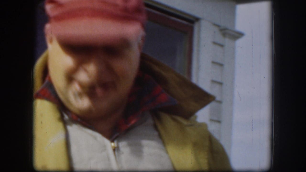 Close view of man in red cap and tan vest near a white building.
