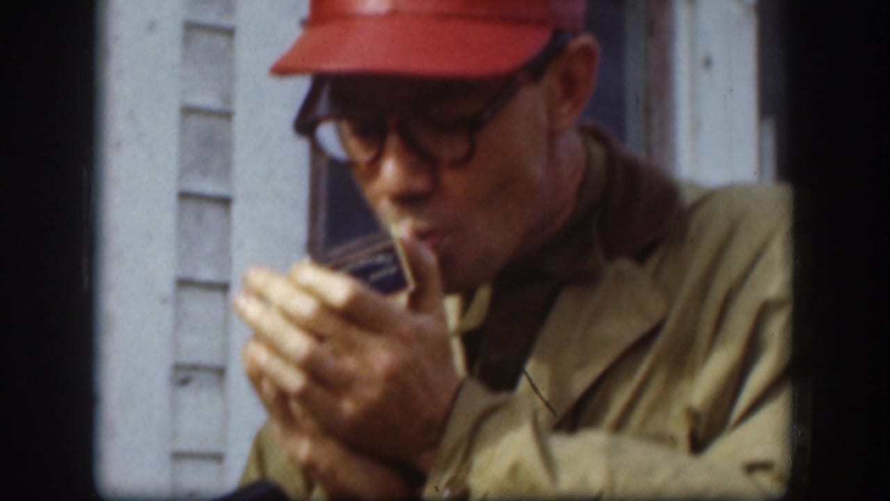 Man in a red cap cups his hands while lighting a cigar.