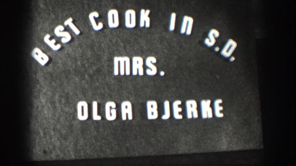 Close 8mm frame of the homemade title card identifying Mrs. Olga Bjerke as Best Cook in S.D.