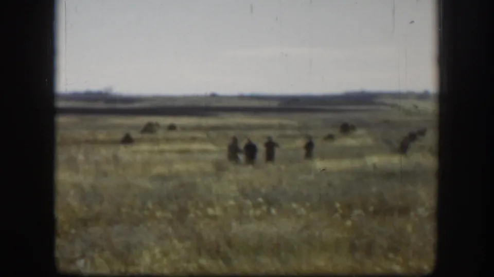 The final frame holds on distant people in a broad Kansas field, with soft focus and visible 8mm film texture.