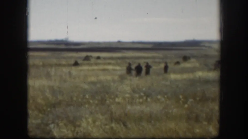 Small figures of hunters appear in a Kansas prairie field in 1958, seen from a distance through soft 8mm home-movie framing.