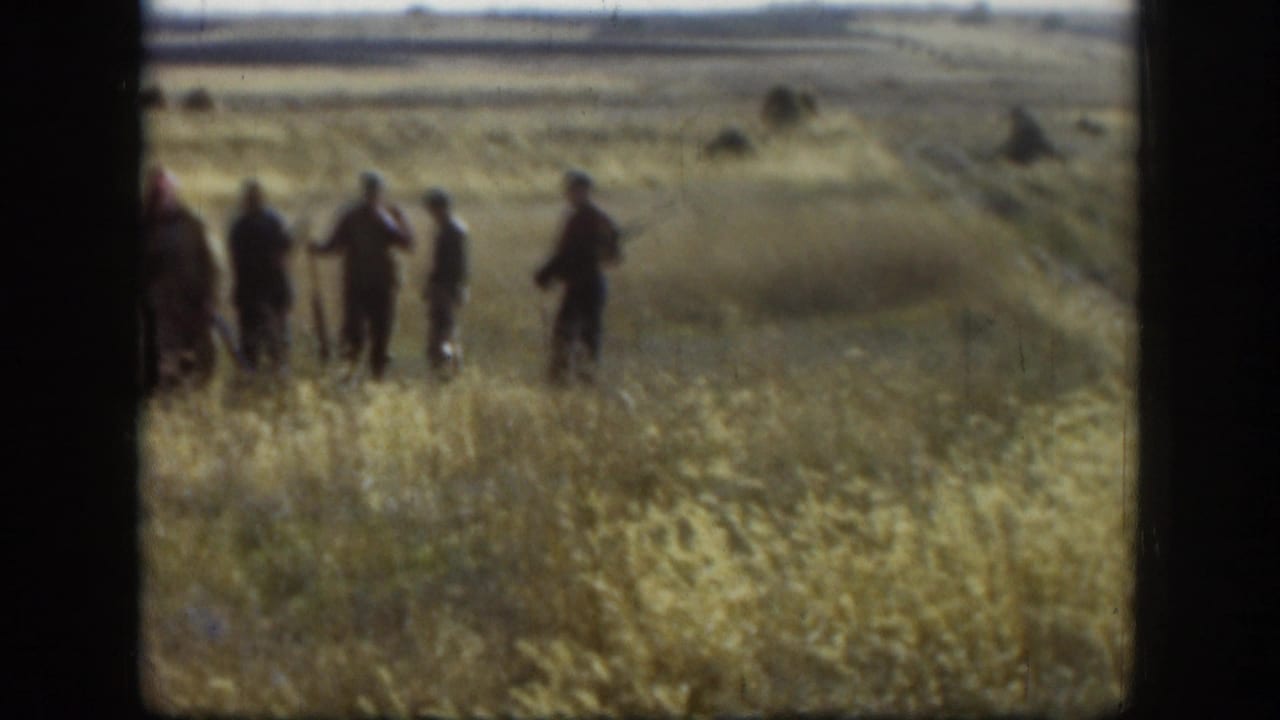 A small hunting party moves through a windy Kansas field, with hats and long guns visible in the faded 1958 8mm frame.