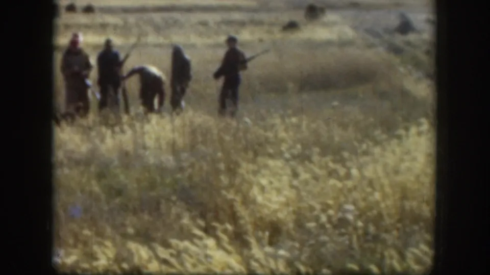 Hunters in hats stand and bend in a Kansas prairie field, their figures softened by grain and distance in the 1958 8mm footage.