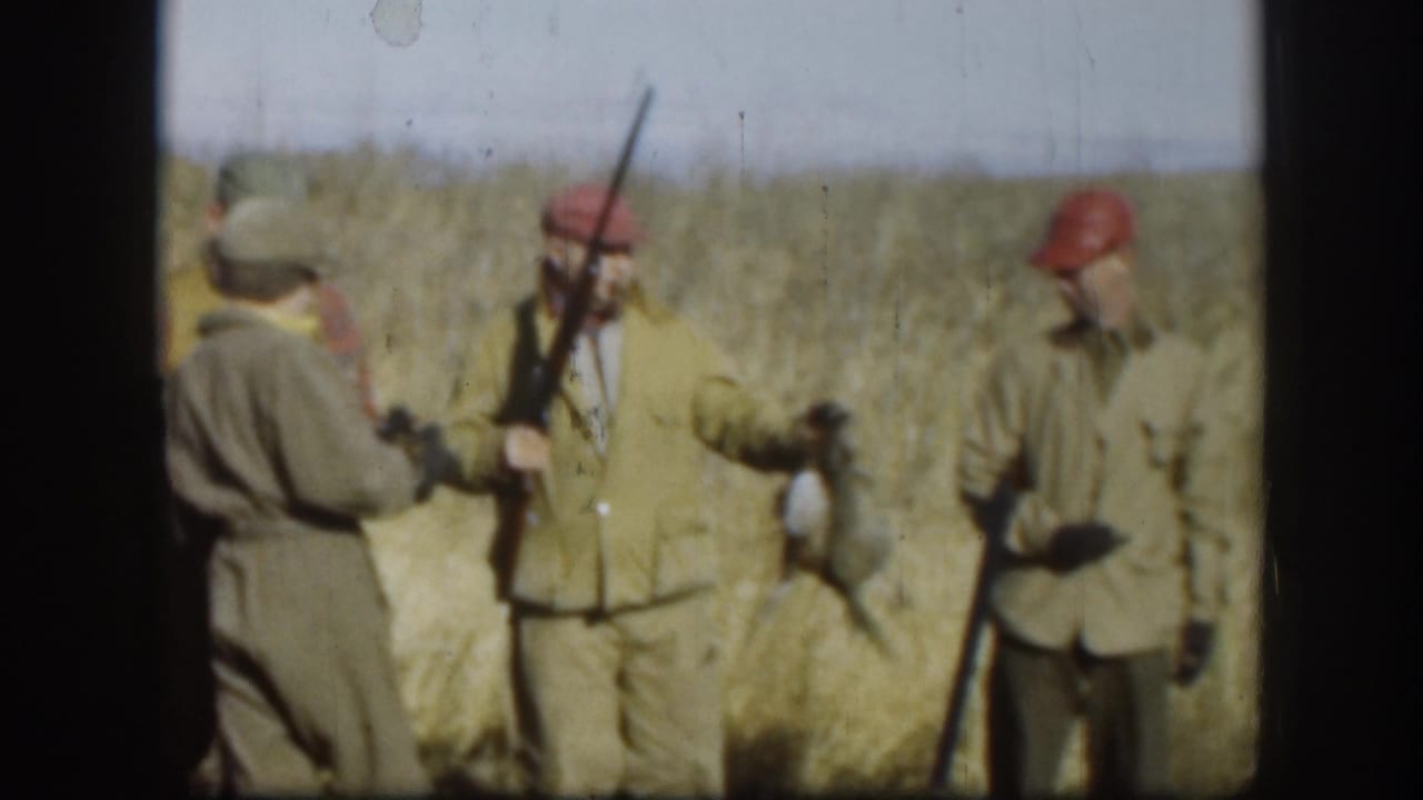Adult hunters in a Kansas field stand with shotguns and wild ducks, wearing caps, vests, and jackets typical of a mid-century outing.