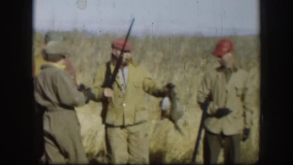 Adult hunters in a Kansas field stand with shotguns and wild ducks, wearing caps, vests, and jackets typical of a mid-century outing.