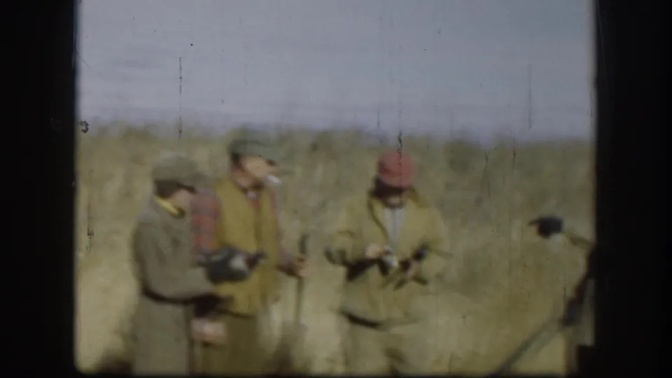 Several adult men in 1958 Kansas home-movie footage gather in a dry field, holding rifles and looking toward a possible game bird.