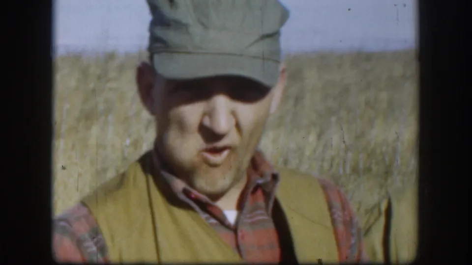 Adult hunter in cap and vest faces the camera in a Kansas field, filmed on 8mm in 1958.