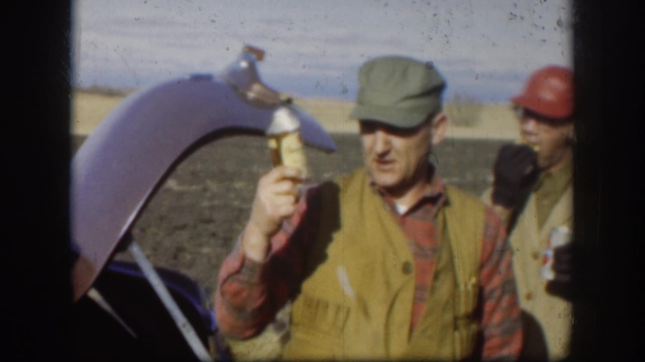A Kansas hunting-trip frame from 1958 shows a man in a green cap holding a drink near an open trunk, with another hunter partly visible.
