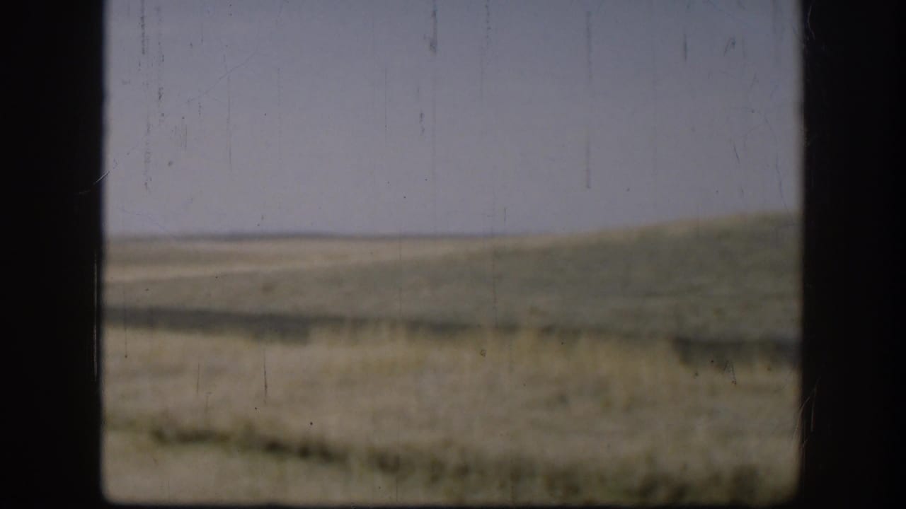1958 Kansas home-movie frame showing pale sky, muted grassland, and low hills divided by a dark window or vehicle frame.