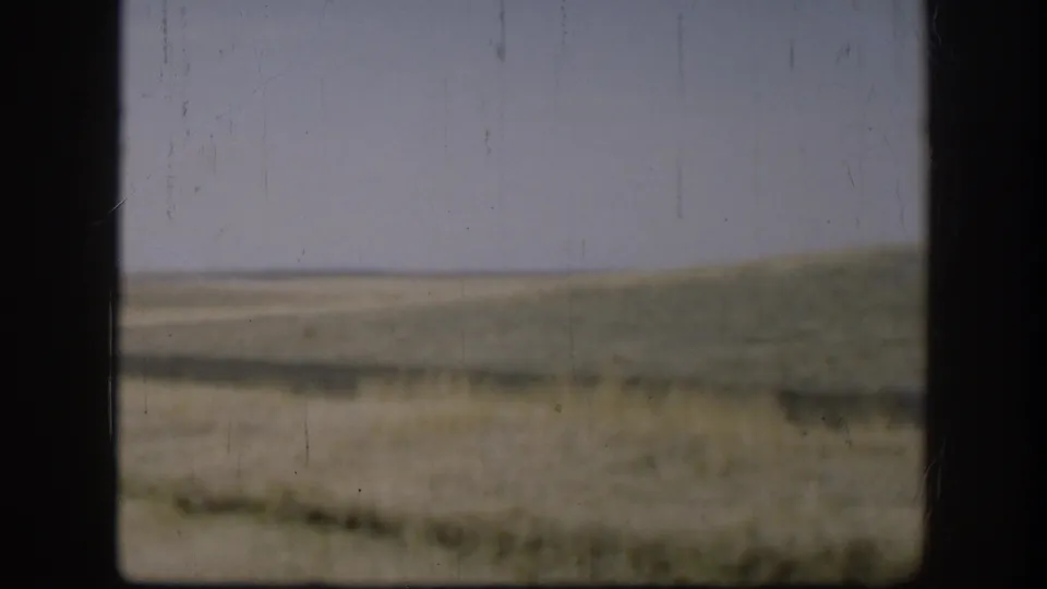 1958 Kansas home-movie frame showing pale sky, muted grassland, and low hills divided by a dark window or vehicle frame.