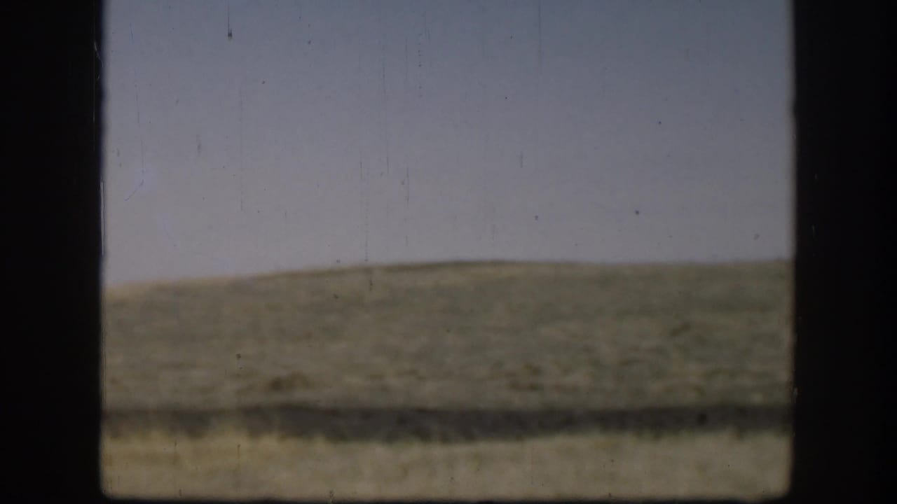 Kansas rural view from 1958 with green-brown hills, pale sky, and a heavy dark frame crossing the foreground.