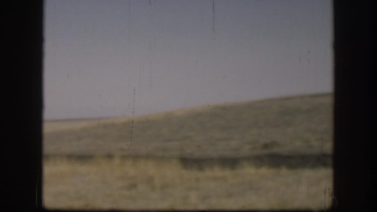 1958 Kansas landscape frame showing a low grassy ridge, open field, pale sky, and dark frame bars across the view.