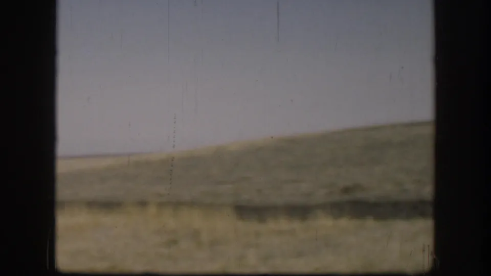 1958 Kansas landscape frame showing a low grassy ridge, open field, pale sky, and dark frame bars across the view.