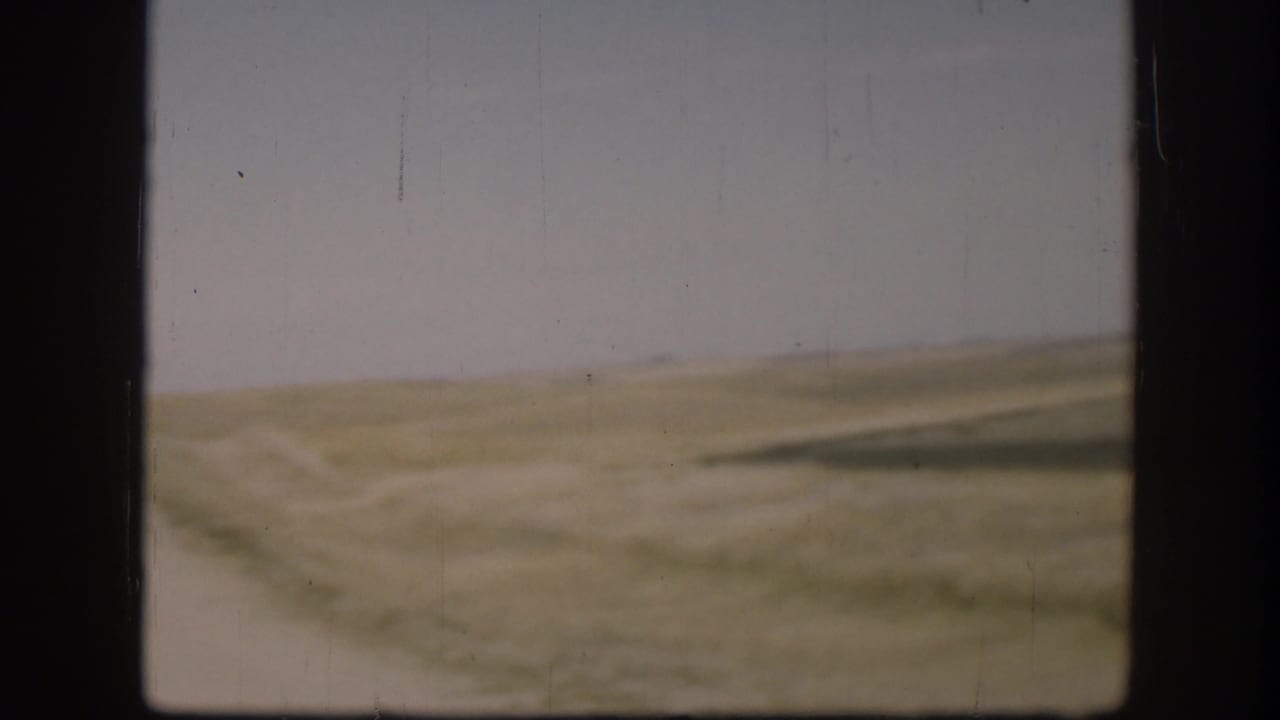 Kansas home-movie view from 1958 showing a faint clay road or track through open grassland and low hills.