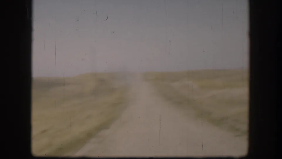 1958 Kansas 8mm frame showing a pale dirt road through open rural fields with soft focus and visible film scratches.