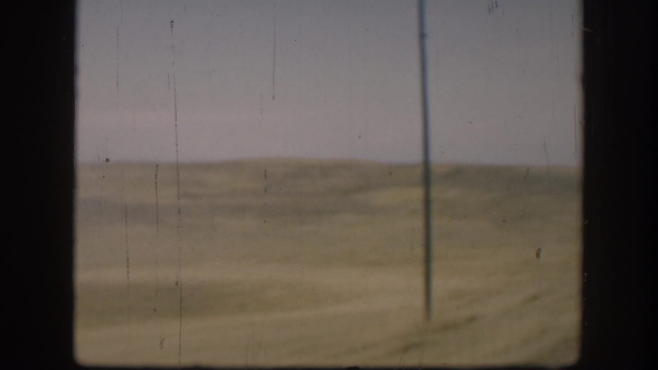 1958 Kansas rural field view with a lone utility pole, flat grassland, hazy sky, and 8mm film wear.