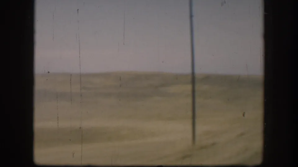 1958 Kansas rural field view with a lone utility pole, flat grassland, hazy sky, and 8mm film wear.