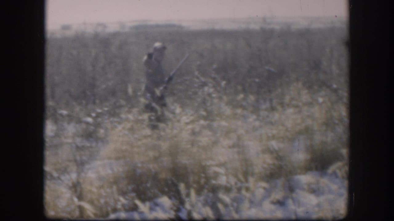 Hunter walking through a dry grassy field with a shotgun.