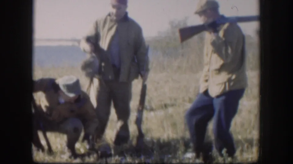 Adult hunters, a dog, and game birds are visible in a 1958 Kansas hunting scene shot on 8mm film.
