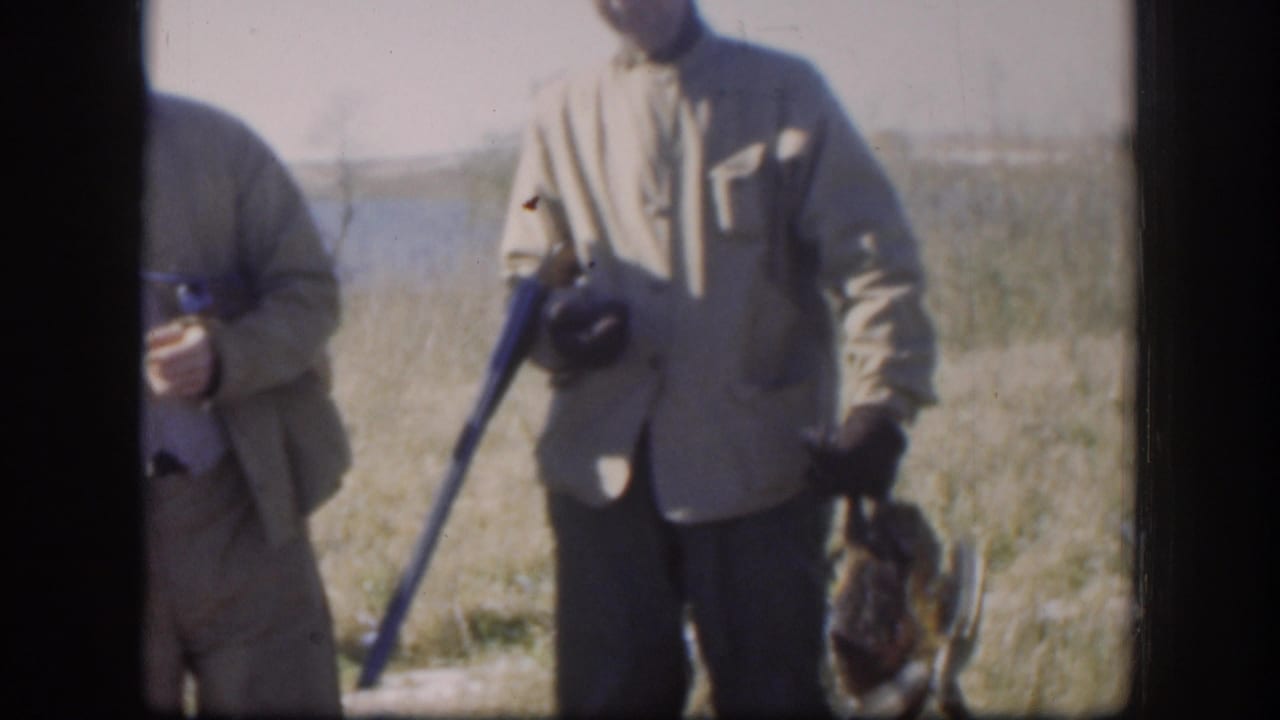 Hunters in field clothing stand with long guns and birds beside a grassy wetland.