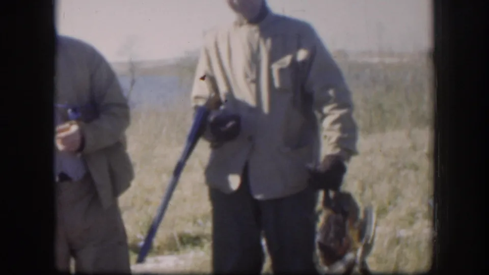 Adult hunters in 1958 Kansas appear beside grass and water, holding shotguns and birds while facing the home-movie camera.