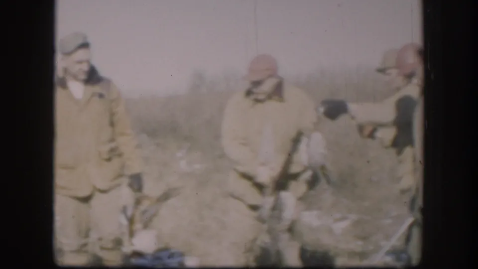 Adult hunters in 1958 Kansas stand together with shotguns and game birds, framed by dry grass and soft 8mm color.