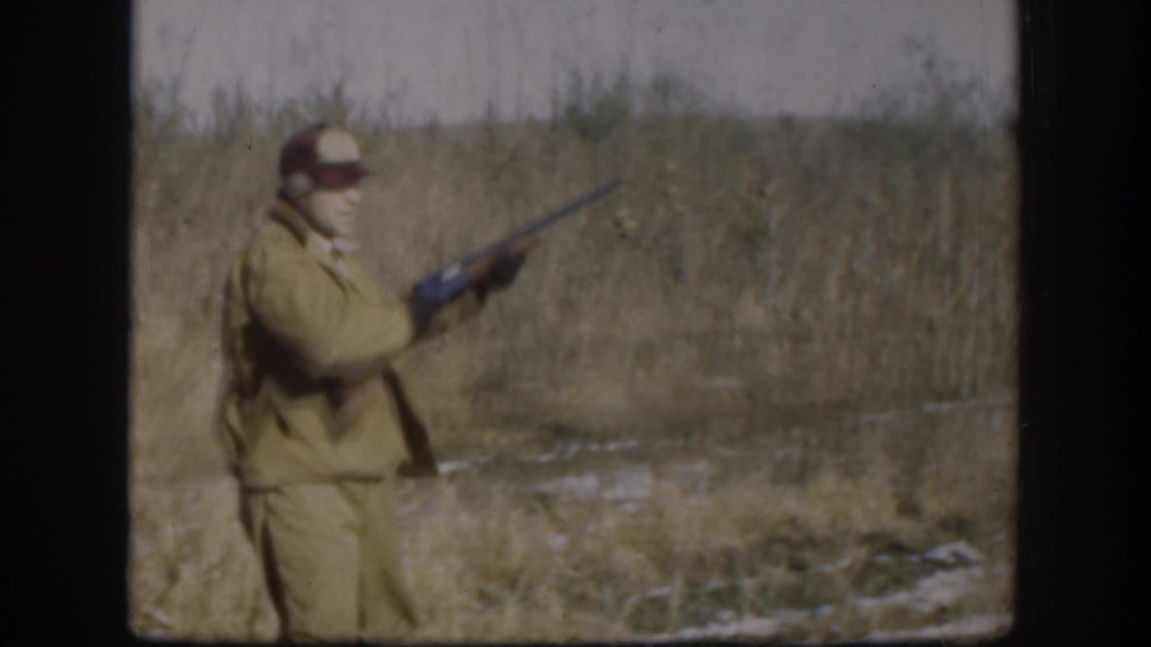 1958 Kansas frame showing a man in a red cap and tan hunting clothes holding a rifle in a grassy field.