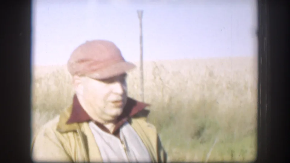 1958 Kansas home-movie frame showing an adult man in a red cap and jacket against open grassland.