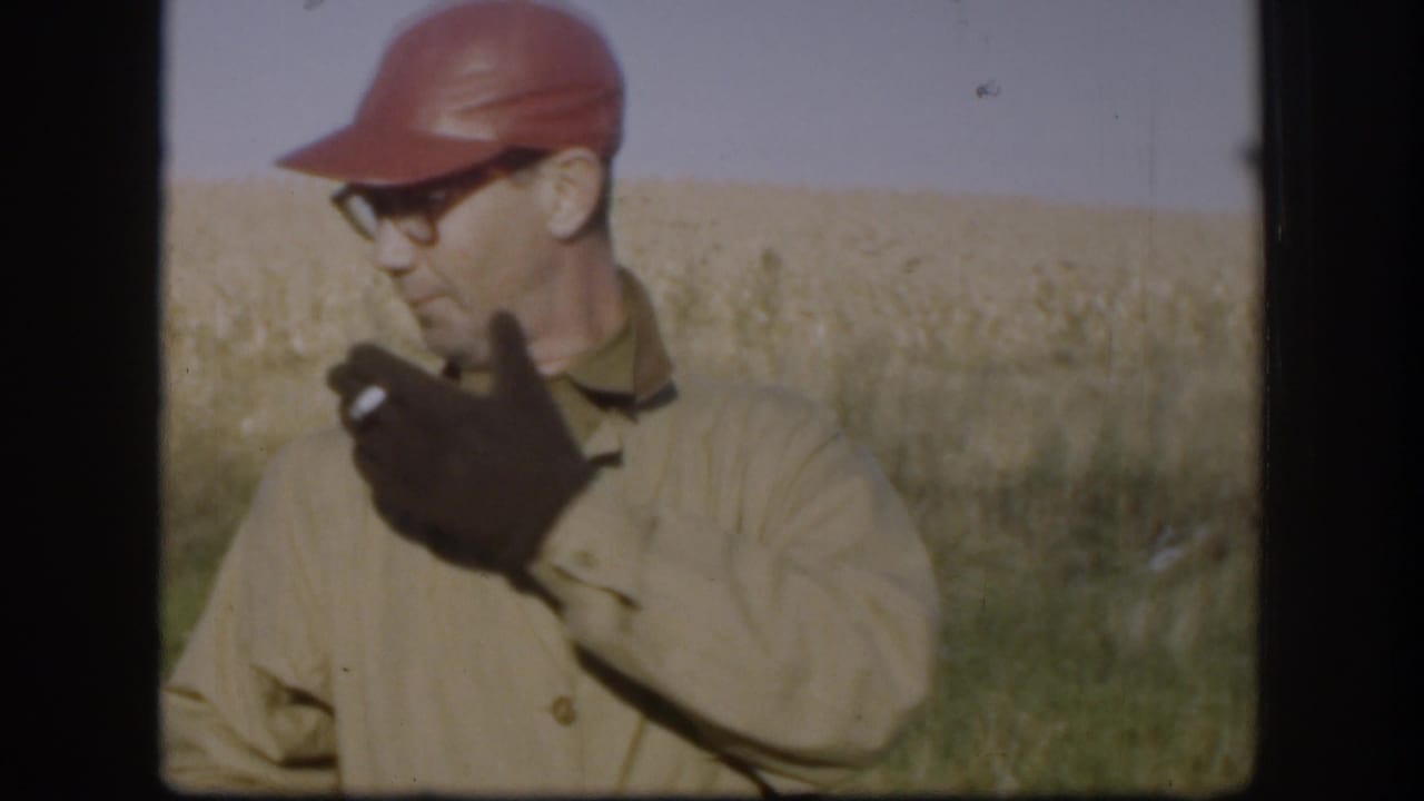 Man in red cap and glasses smoking in a field.