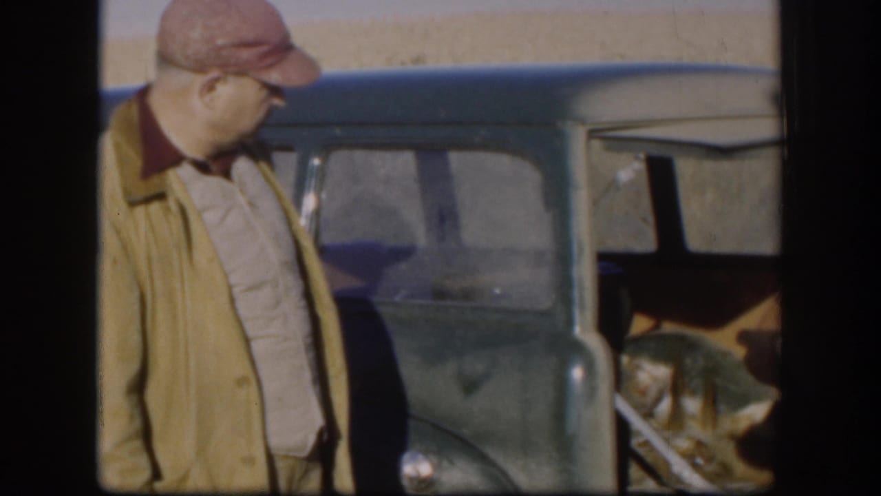 Man in red cap stands beside an open vintage car.