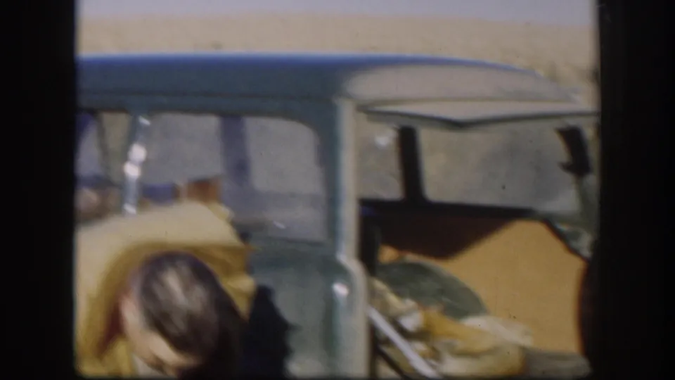 A man bends near the open green car as another person is partly visible in 1958 Kansas rural footage.