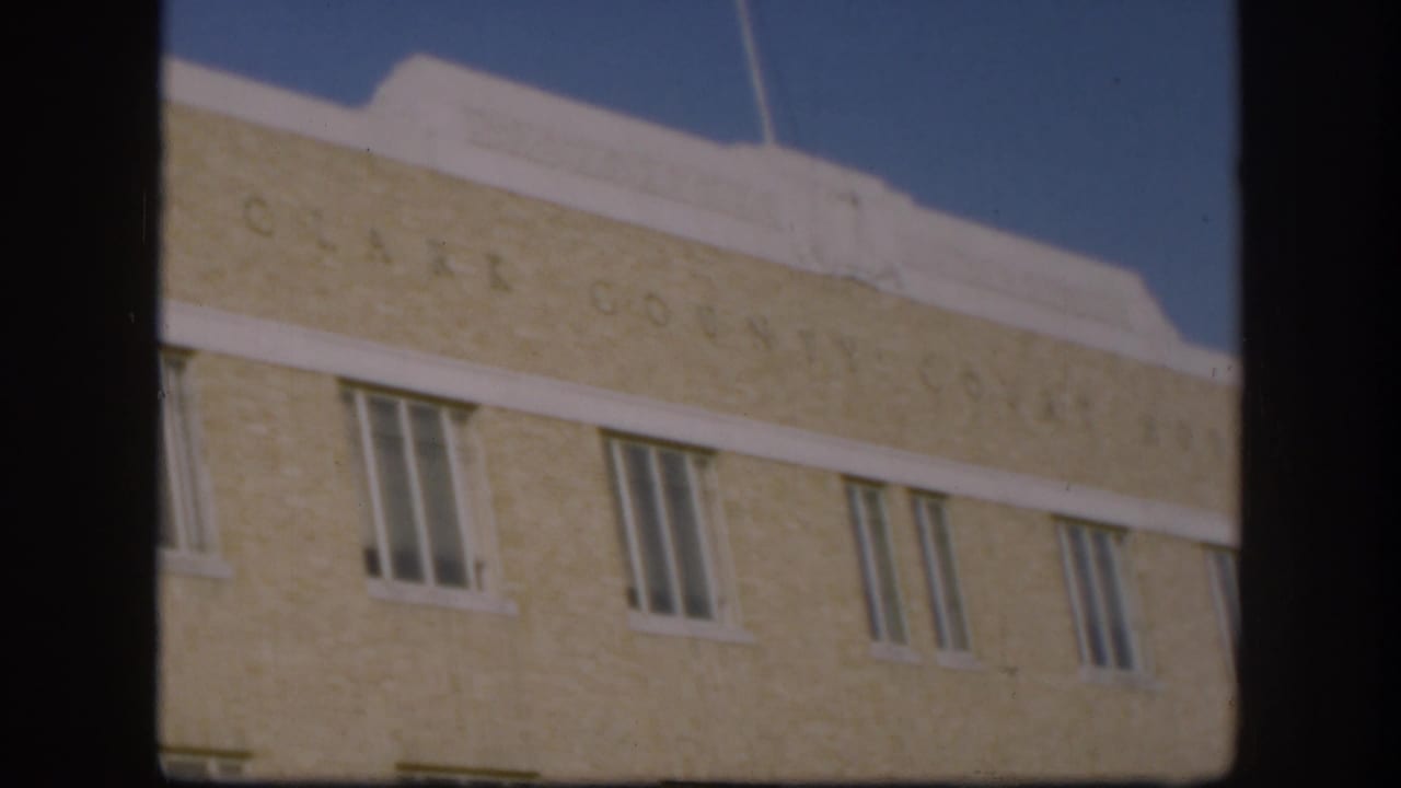 1958 Kansas frame of the Clark County Courthouse roofline and upper facade, with faint lettering, white trim, windows, and blue sky.