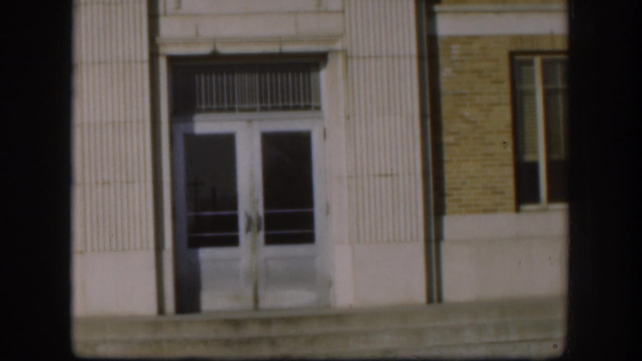 Kansas courthouse entrance with double glass doors, vertical fluted trim, brickwork, and concrete steps in 1958 home-movie footage.