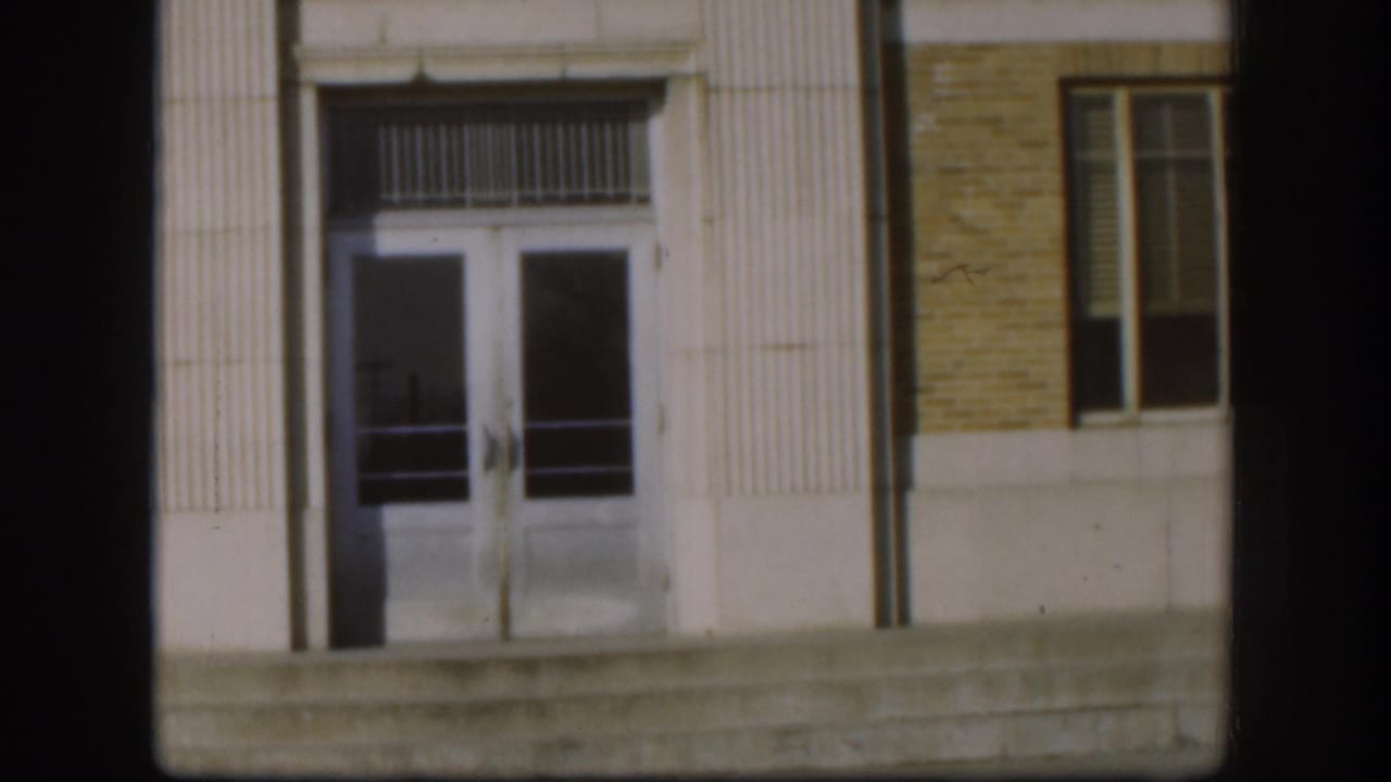 1958 Kansas courthouse doorway seen closer, showing glass double doors, concrete steps, brick facade, and a tall side window.
