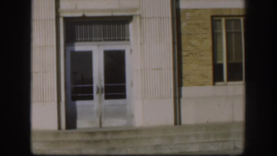 1958 Kansas courthouse doorway seen closer, showing glass double doors, concrete steps, brick facade, and a tall side window.