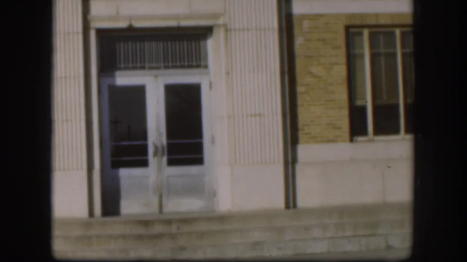 Kansas courthouse entrance detail in 1958 8mm footage, with double glass doors, fluted trim, brick wall, and concrete steps.