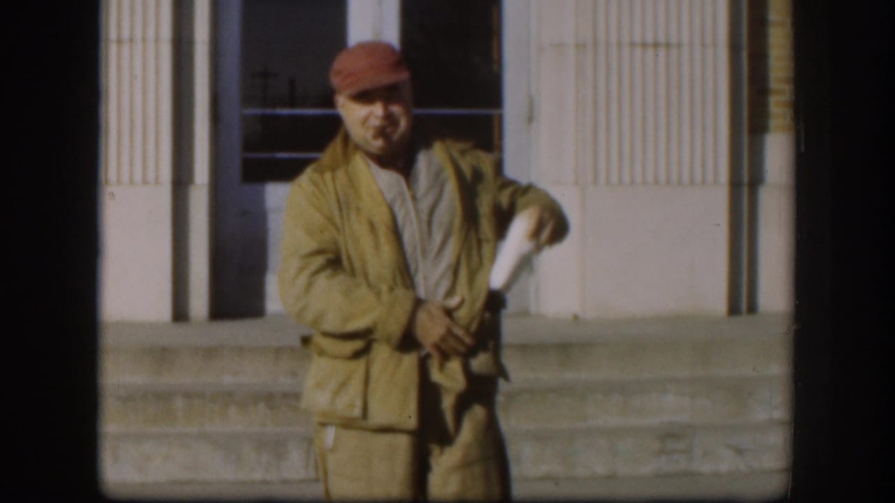 In the final Kansas 1958 still, the man stands closer to camera, handling a small item near his jacket with the building behind him.