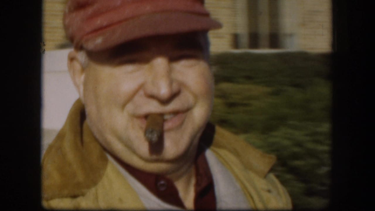 Close view of a smiling man in a red cap with a cigar in his mouth.