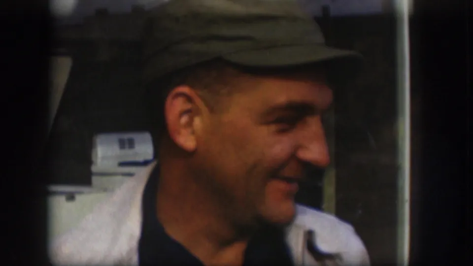 Close 1958 Kansas home-movie view of the man smiling in profile, wearing a cap and light jacket, with soft focus and dark film edges.